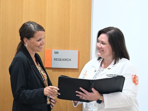 Woman in dark suit holding a padfolio with a woman in a white coat