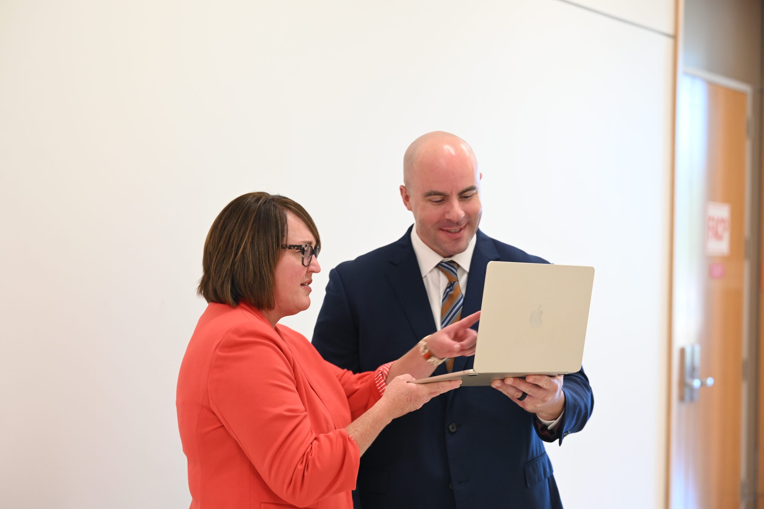 Woman in orange blazer holding laptop with man in dark suit