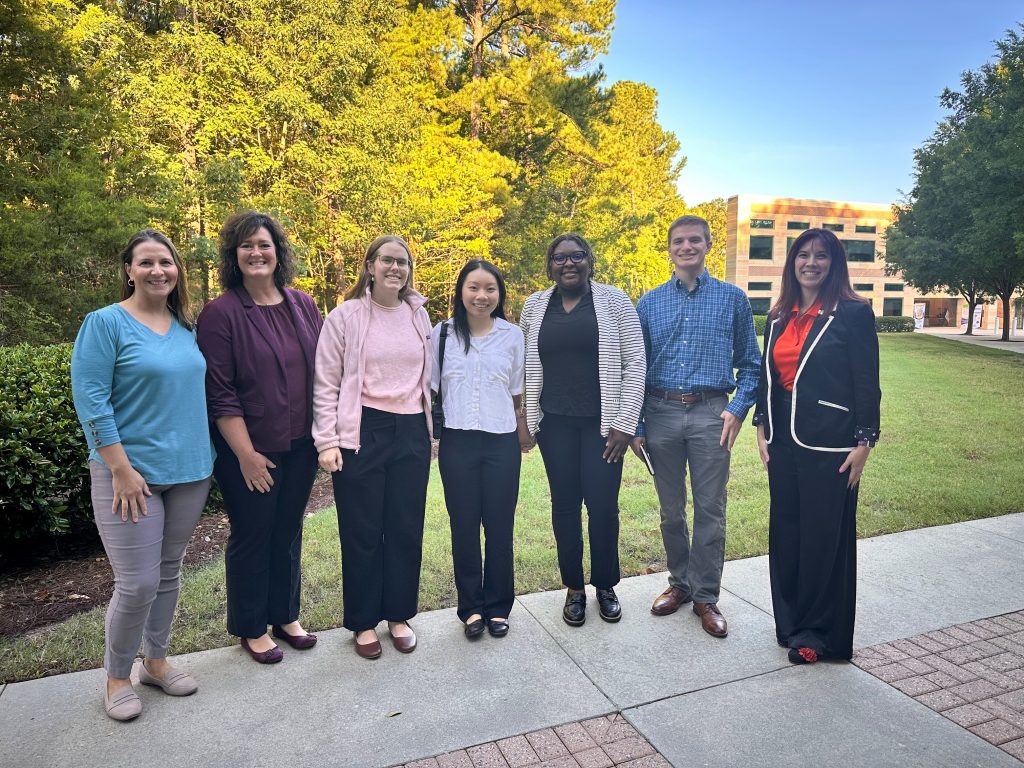 Three faculty members and four students standing on a sidewalk outside the conference building