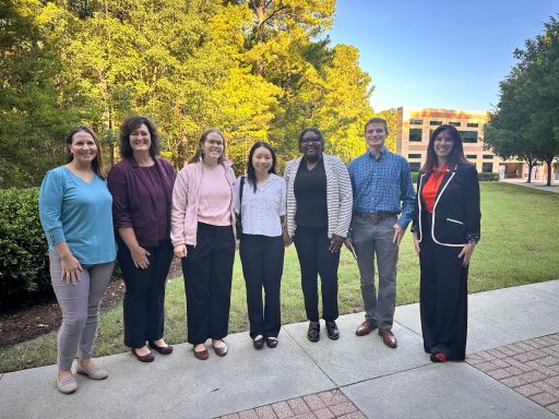 Three faculty members and four students standing on a sidewalk outside the conference building