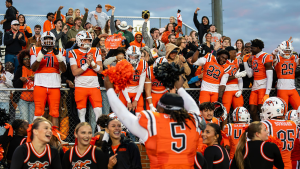 Campbell football players in orange uniforms celebrate with cheering fans and cheerleaders at Barker-Lane Stadium during Homecoming 2026.