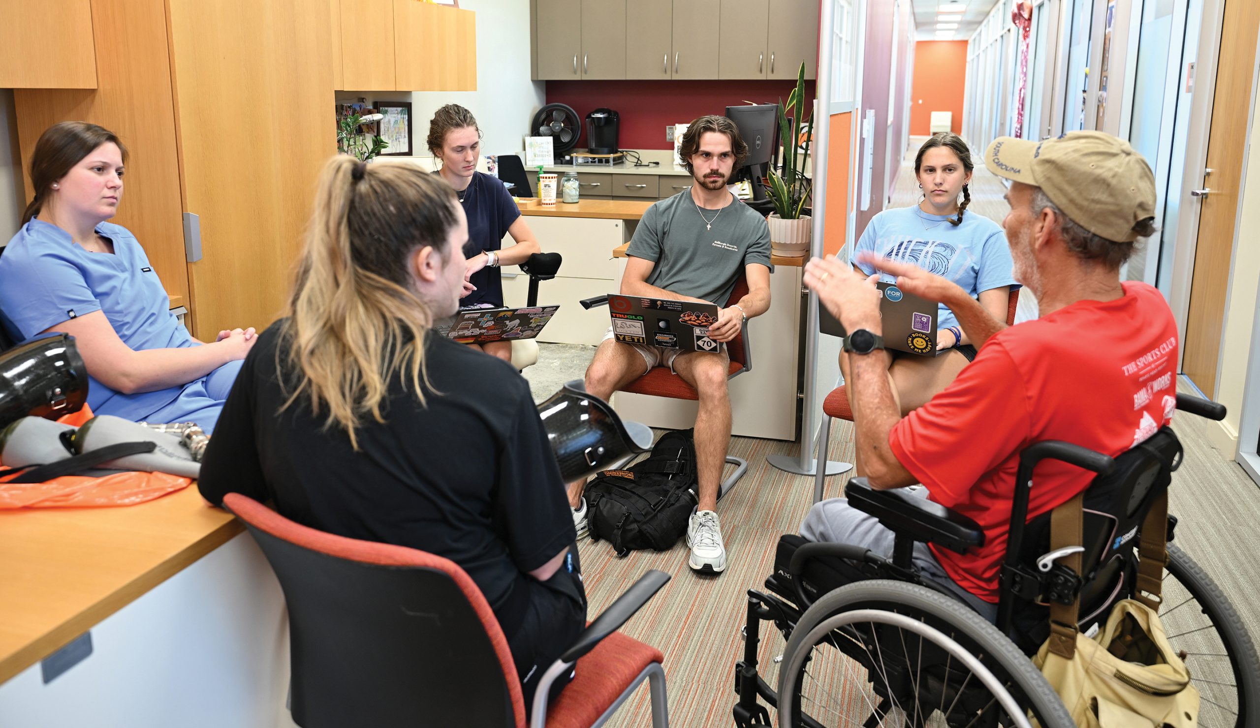 Students meet with a man in a wheelchair to talk about creating prosthetic swimming fins