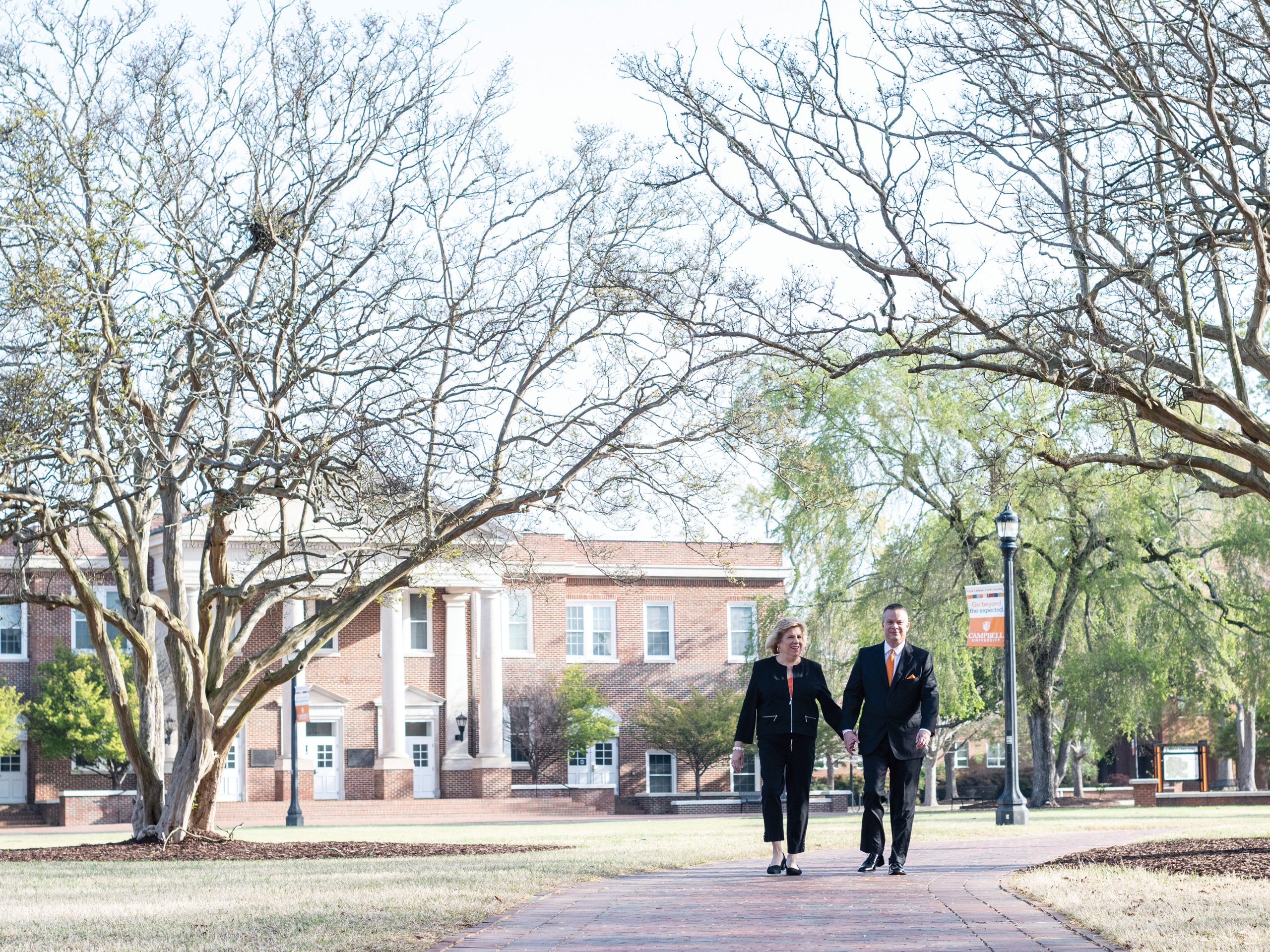 The president and first lady hold hands while walking on campus