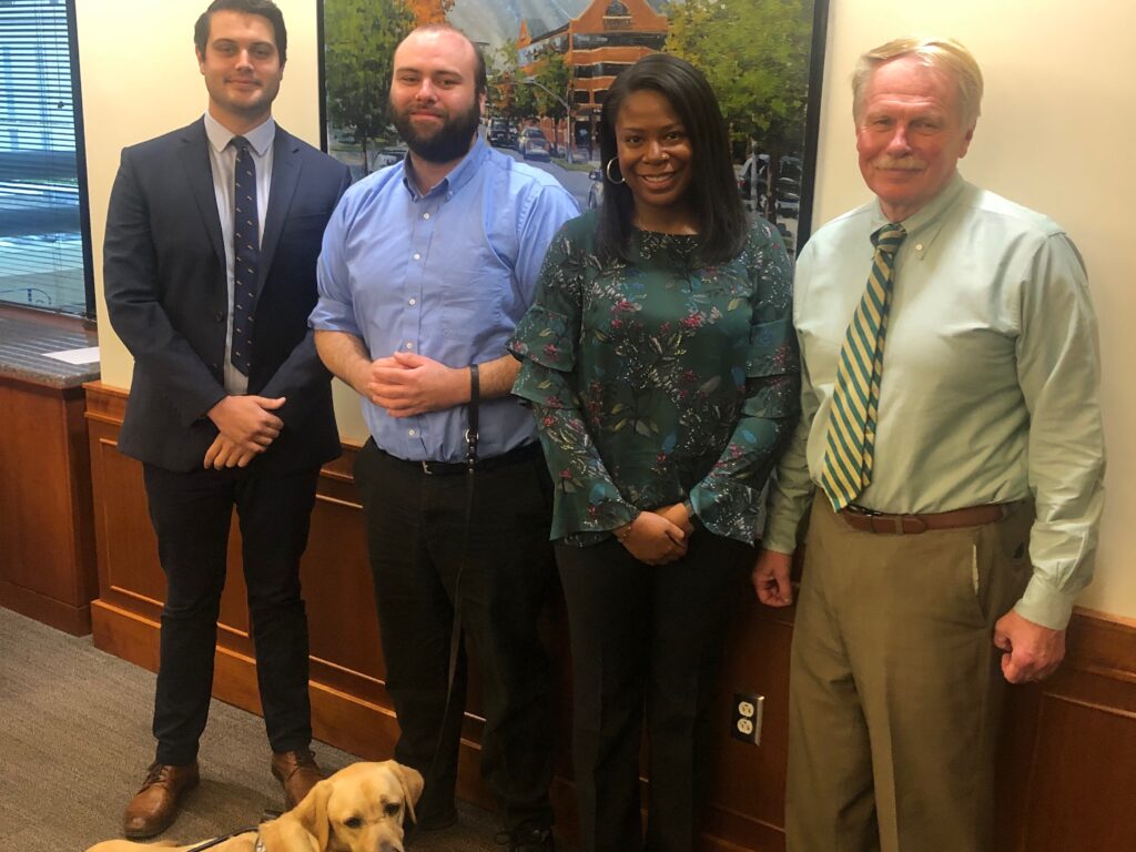 Photo of 2018-19 Wallace Fellows Brennan Cumalander, Cody Davis, his service dog Clark, and Morgan Pierce with Dean Leonard in Dean's Conference Room