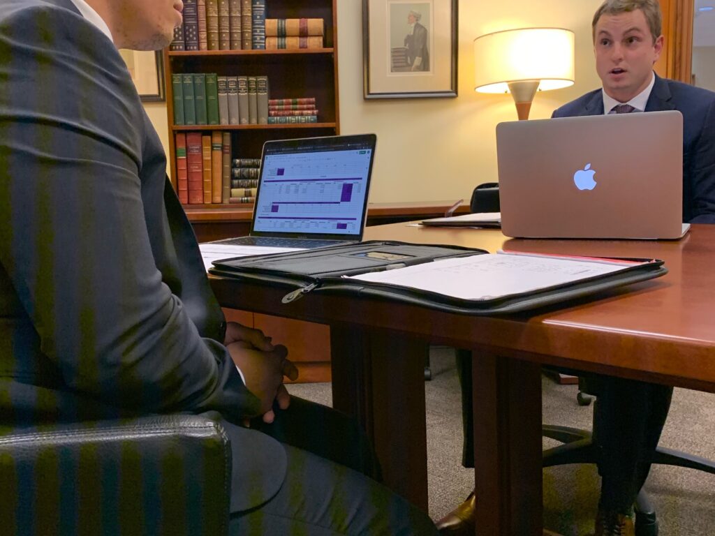 Photo of two male Campbell Law advocates sitting at a table in front of their Apple computers practicing.