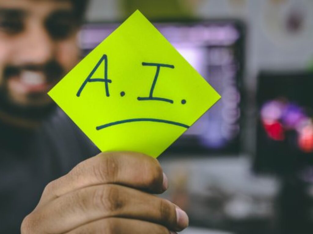 Photo of a man holding a yellow sticky note wit the letters A.I. written on it