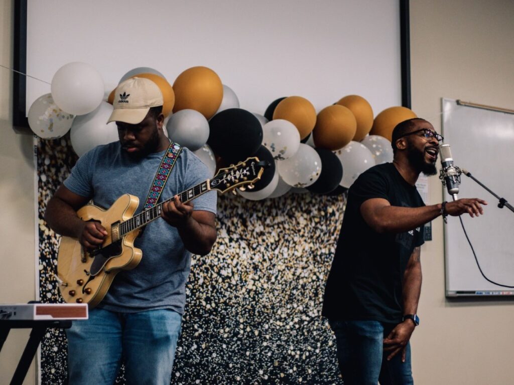 Photo of Brandon Irabor '21 playing guitar and Dean Evin Grant singing in to a mic