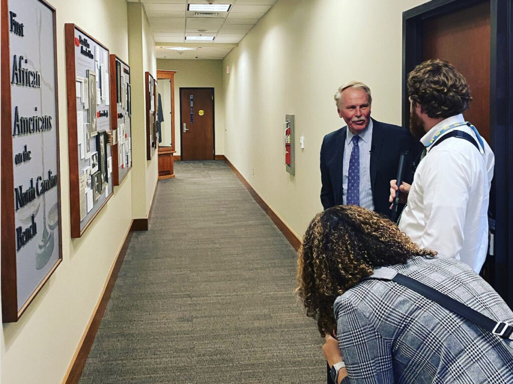 Photo of Dean Leonard being interviewed in front of First NC African American Judges on the Bench