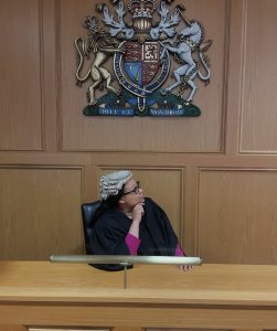 Photo of Erica Howard posing on a judge's bench in a robe with a white wig in Nottingham