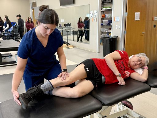 Female DPT student wearing navy blue scrubs working on a patient who is lying on a table on her side.