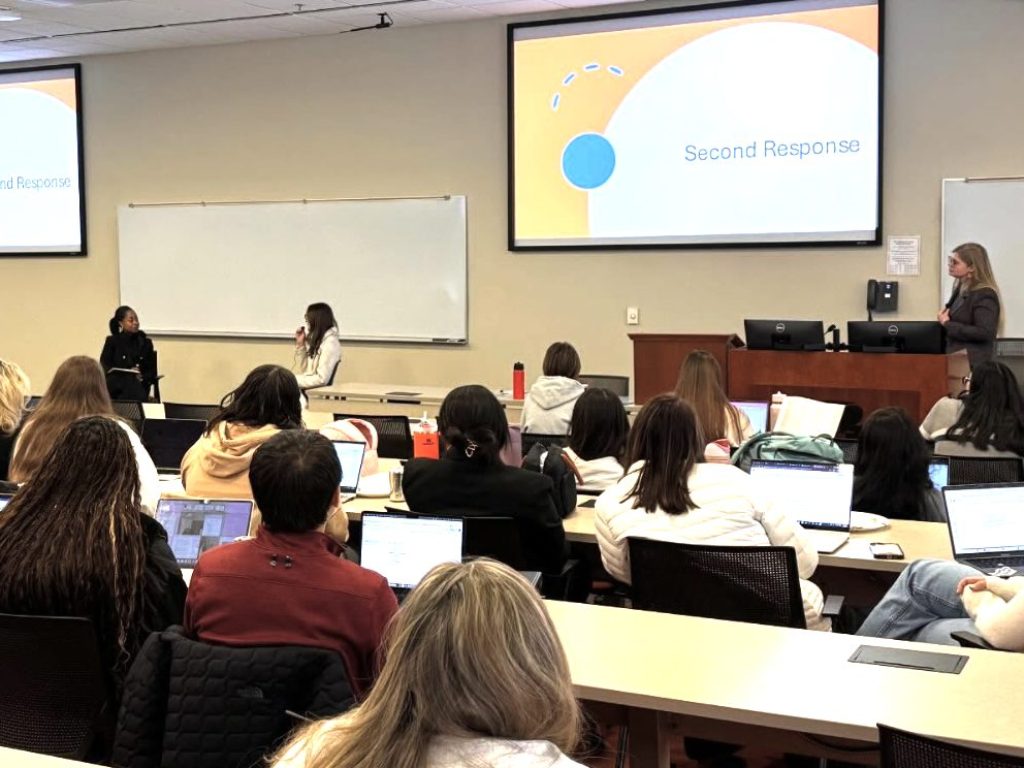 Photo of Career Center event where Darrah Perry '25 is doing a mock interview with a law student while Christiana Johnson looks on in front of classroom full of students