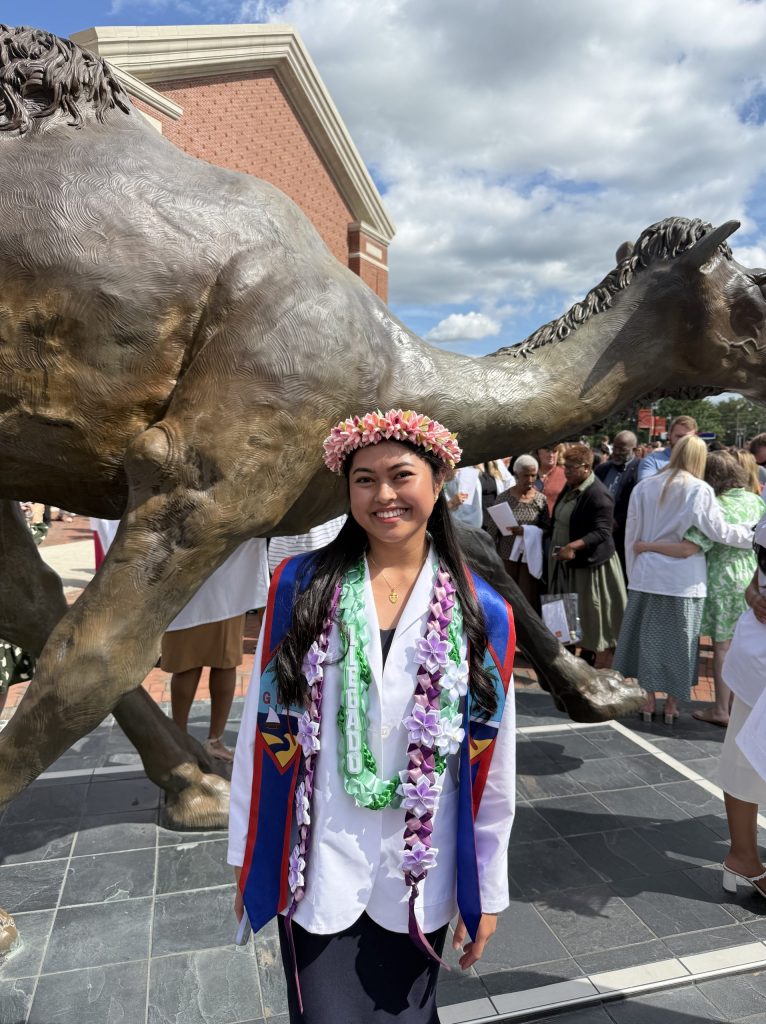 Female DPT student after the white coat ceremony standing in front of the large camel statue on Campbell University's campus
