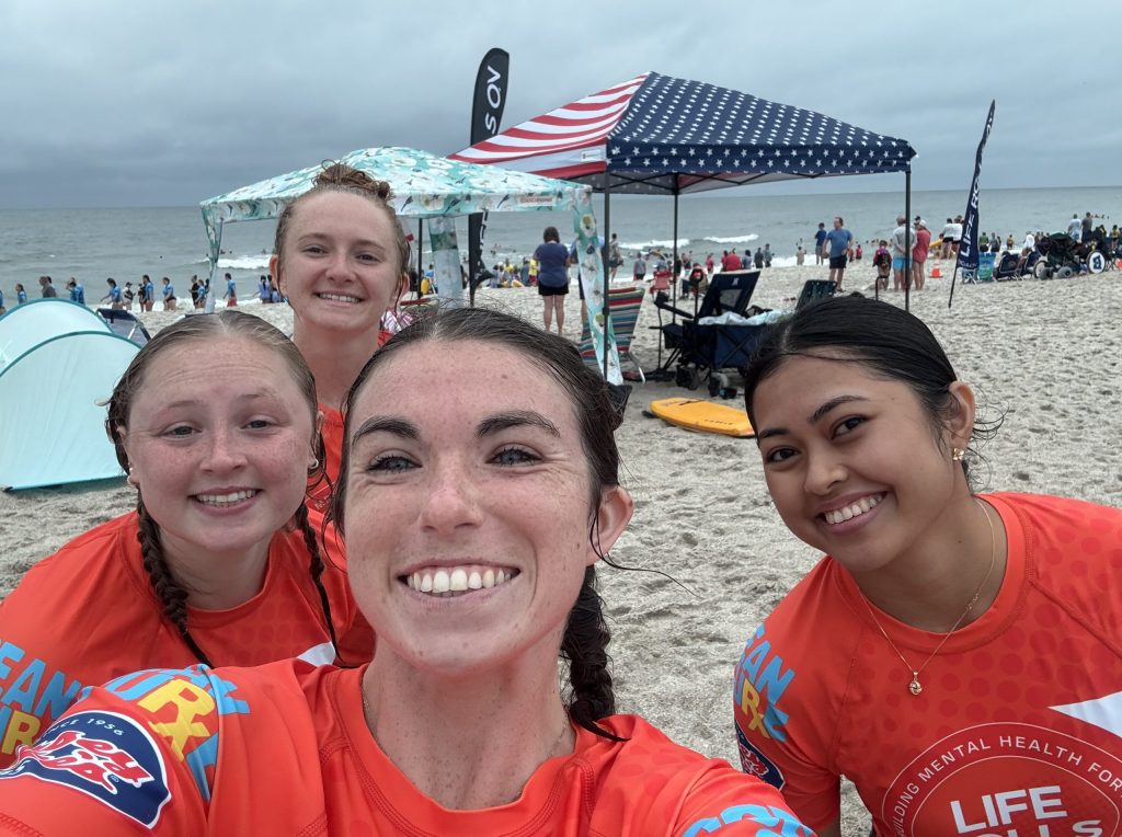 Four female PT students taking a selfie on the beach during a PT event all wearing red shirts