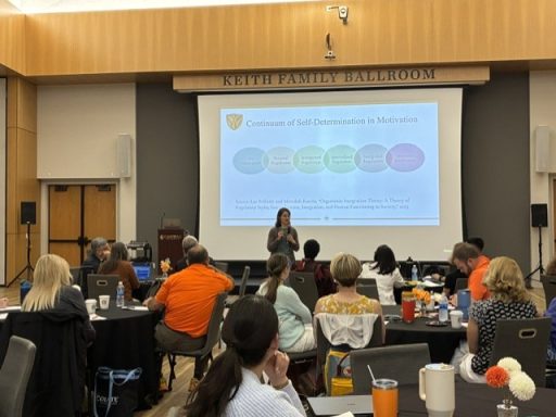 action photo from the curriculum event showing individuals at round tables taking notes and engaged as speaker Dr. Whiting shares about the self-determination in motivation continuum.