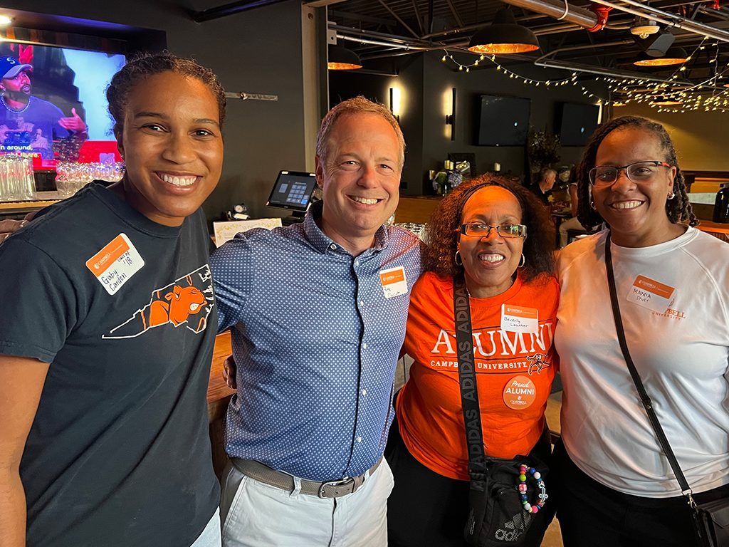 Four individual posing for a photo. All four have name tags while three individuals have Campbell University t-shirts on.