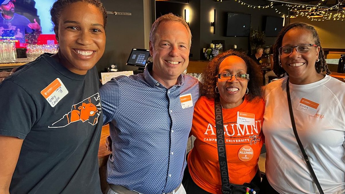 Four individual posing for a photo. All four have name tags while three individuals have Campbell University t-shirts on.