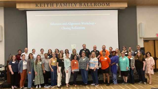 group of faculty and staff from Campbell University in the Student Union ballroom taking a group photo at their curriculum event.
