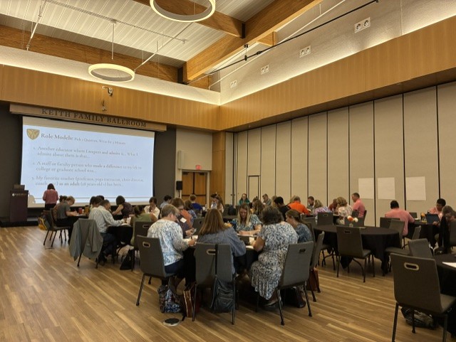 Group of faculty and staff seated at round tables engaged in working at curriculum summit on campus at Campbell