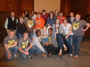 A group of Campbell students and staff pose together during a Campus Worship event at Caswell, with several wearing Campbell shirts and event name tags.