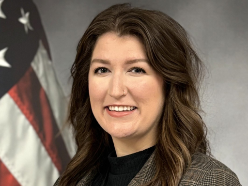 Hannah Byrd Collins poses, smiling for a headshot. An American flag is in the background.