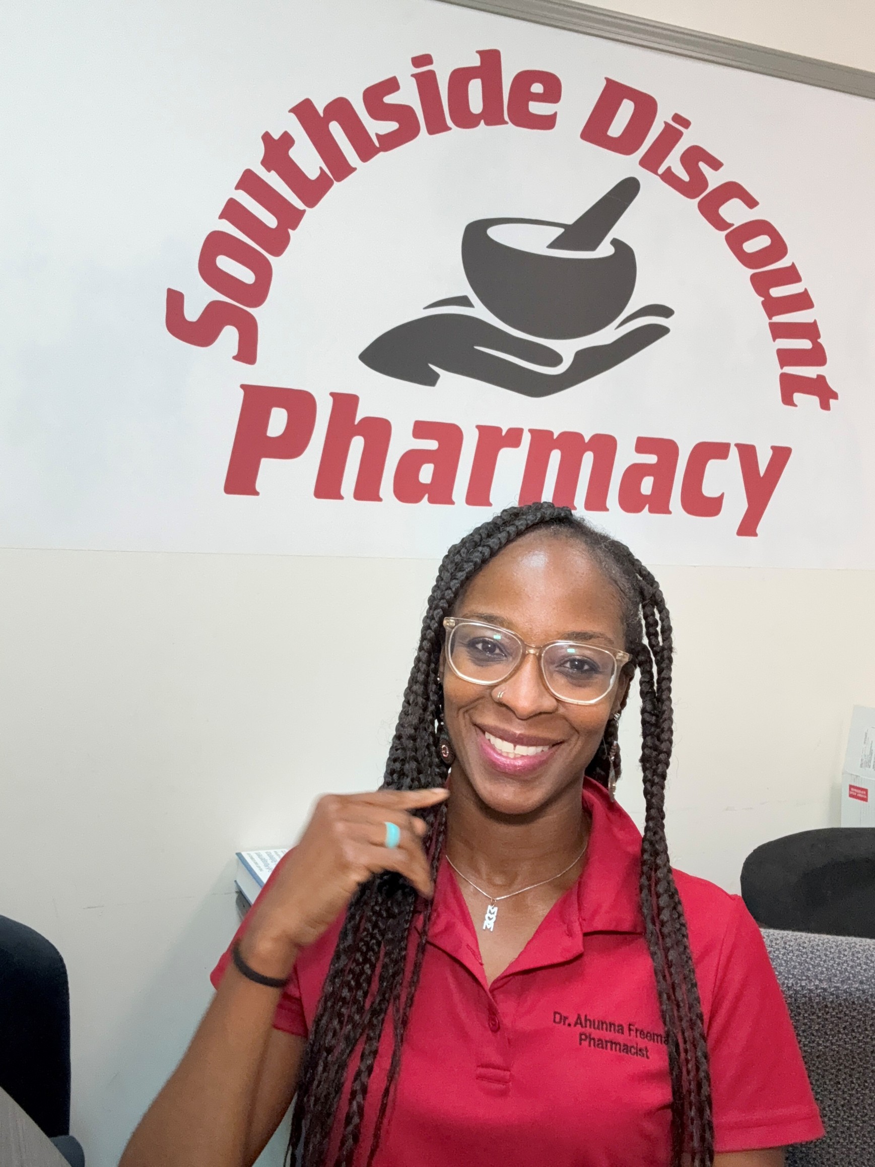 Female with glasses standing inside a pharmacy wearing a red collared shirt.