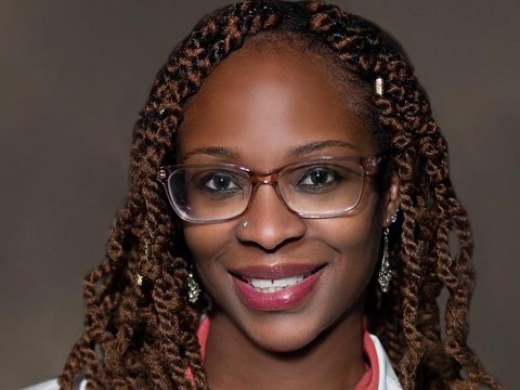 Female with glasses wearing clinical white coat.
