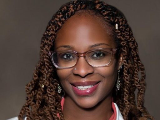 Female with glasses wearing clinical white coat.